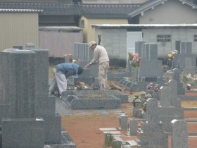 雨の中ベタベタに濡れてしまった石に接着剤を塗っている長良石材さん